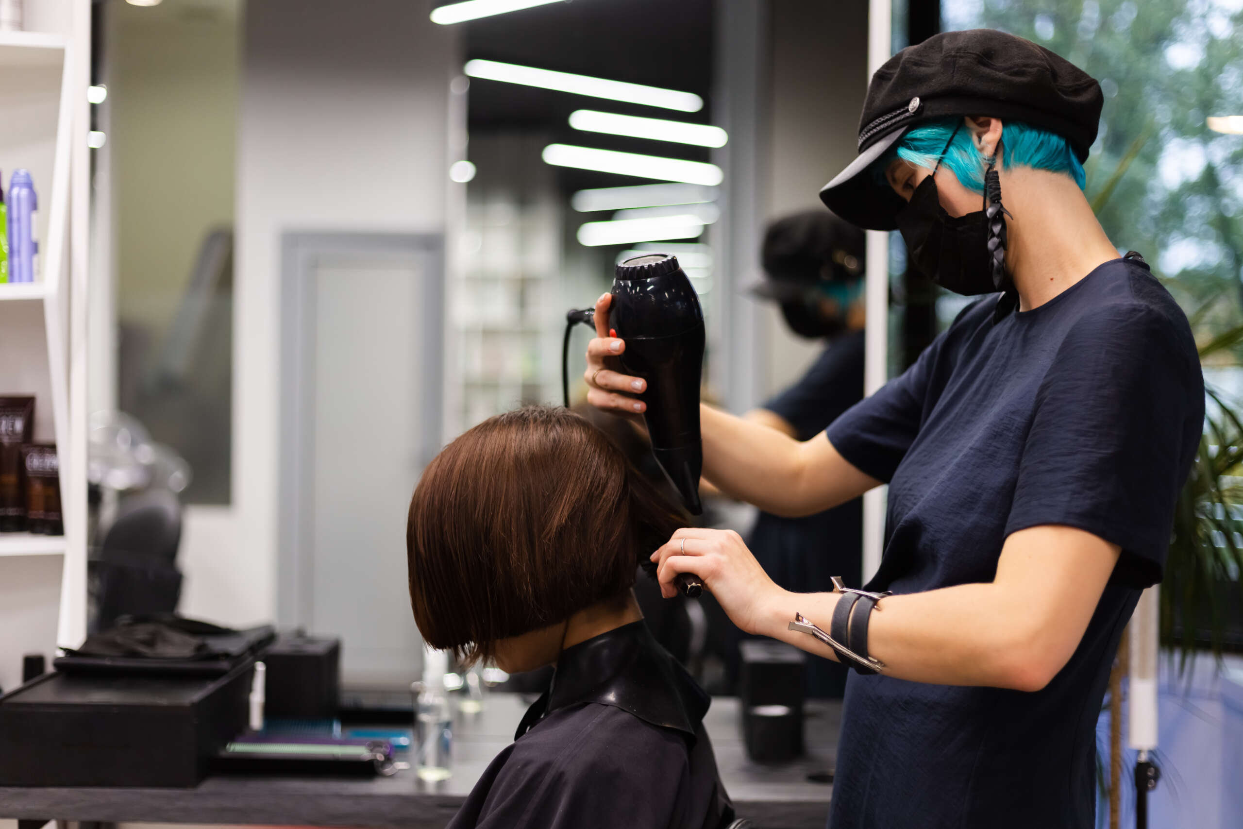 A professional girl hairdresser makes a client haircut. The girl is sitting in a mask in beauty the salon